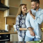 Happy young couple embracing and talking in the kitchen while cooking breakfast at home in the morning